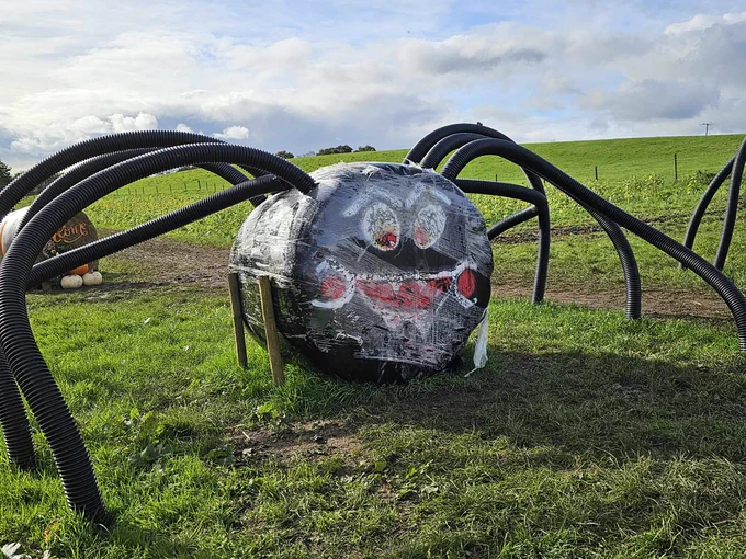 A bale of hay that's been turned in to  spider with pipes for legs.
