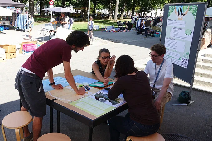 Ein Workshop am mobilen Forschungslabor MobiLab. Menschen unterhalten sich und schauen auf Unterlagen auf einem Tisch. 