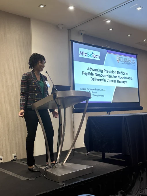 Dr Angela Alexander-Bryant standing at the podium starting her talk titled “Advancing Precision Medicine: Peptide Nanocarriers for Nucleic Acid Delivery in Cancer Therapy”