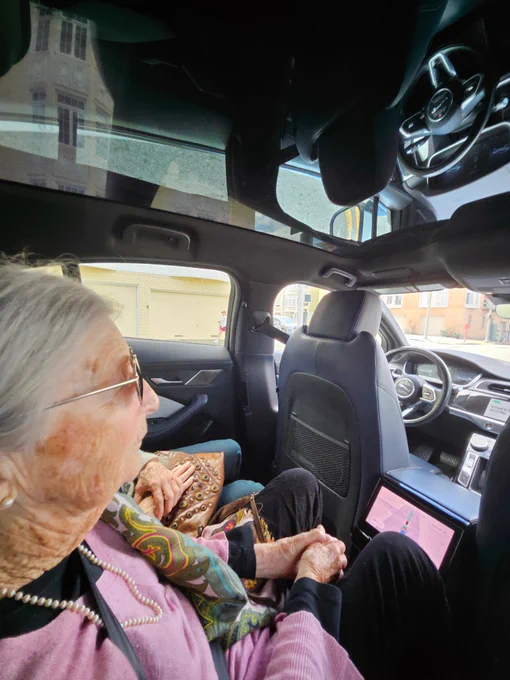 Grandma in the backseat of a moving Waymo robotaxi, with nobody in the driver's seat. Fully driverless!