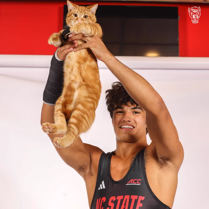 NC State wrestler, Matty Singleton, holds his orange tabby cat to the air like Simba from Disney's Lion King. The cat doesn't seem to care. 