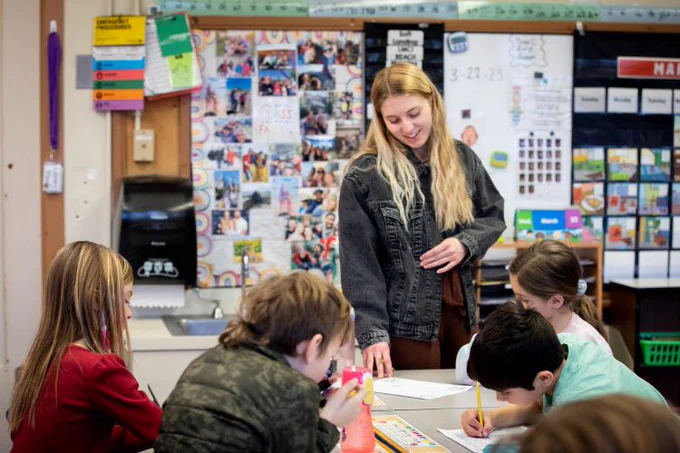 Young teacher interacting with elementary students at a table in a colorful classroom