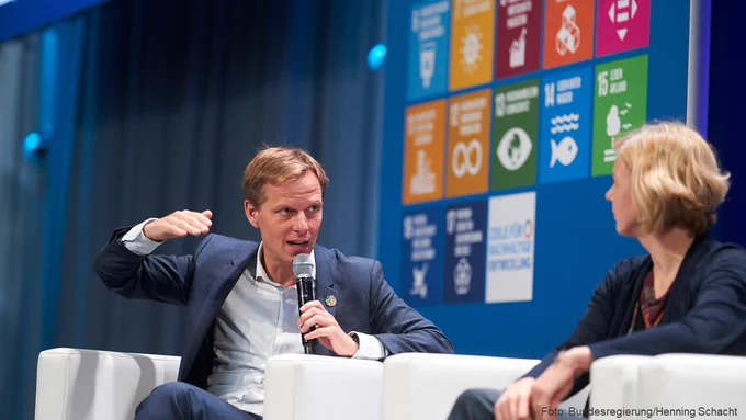 Auf dem Podium der Dialogkonferenz spricht Ratsmitglied Kai Niebert. Im Hintergrund sind die SDG-Tafeln zu sehen.