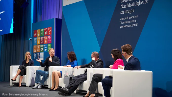 Auf dem Podium der Dialogkonferenz spricht Ratsmitglied Zarah Bruhn u.a. mit Sänger Peter Fox und Staatsministerin Sarah Ryglewski über soziale Innovationen für mehr Nachhaltigkeit. Im Hintergrund sind die SDG-Tafeln und der Schriftzug "Deutsche Nachhaltigkeitsstrategie - Zukunft gestalten - Transformation gemeinsam, jetzt!" zu sehen.