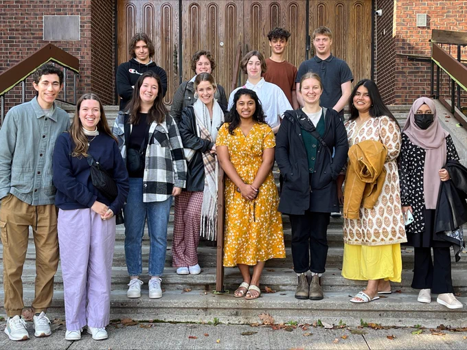 Group photo of university students standing on steps, in front of the large, wooden doors of a synagogue.