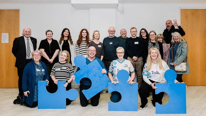 A group photo of participants who attended the Creating Hope With Peer Support: The Power of Lived Experience Networking Day yesterday. Also features four giant blue jigsaw pieces.