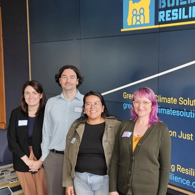 Four people standing in front of a big Building Resilience sign, Climate Solutions, Building Resilience, OJTA, and Zero Coalition.