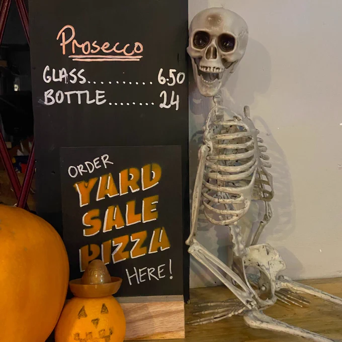 a skeleton on the pleasance bar by a sign that says 'order yard sale pizza here'