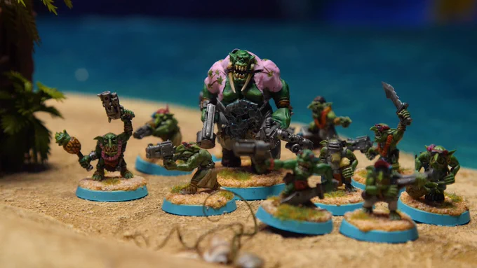 An army of minitaure orcs gather on the shore of a beach. One orc is much larger than the others. 