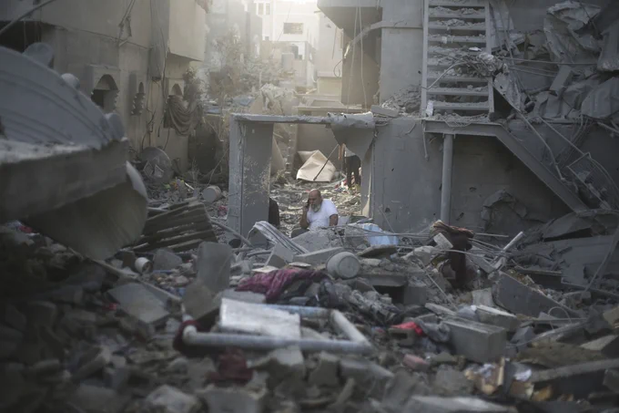 A person sits among a huge pile of debris, following a missile strike, speaking into a cell phone.
