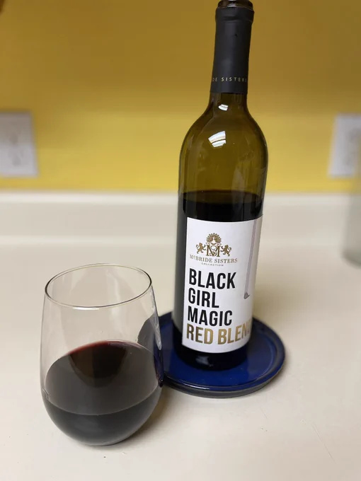 Picture of an opened bottle of wine with a stemless glass filled with some of the wine.  The name of the wine is Black Girl Magic Red Blend