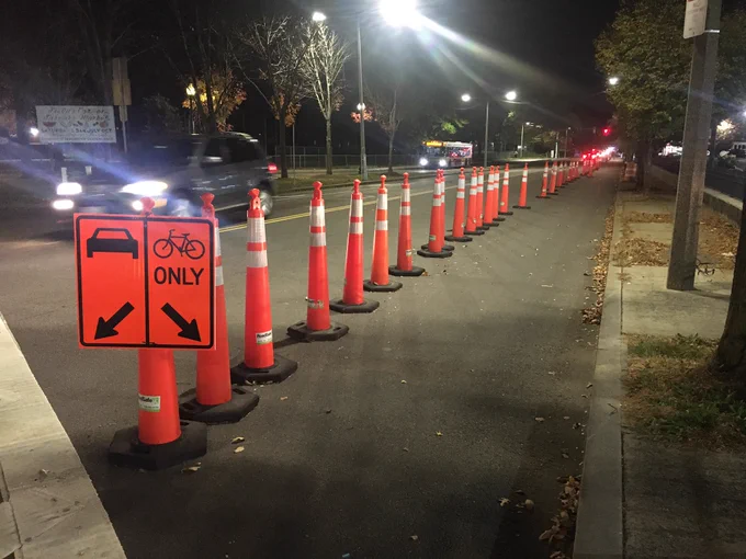 A wide bike lane has been demarcated on a street with tall, orange safety cones and a sign directing cars to keep left and bikes “only” to keep right.