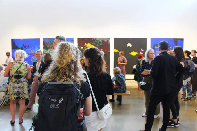 People at an exhibition launch event admiring the artworks displayed on the walls and chatting with one another.