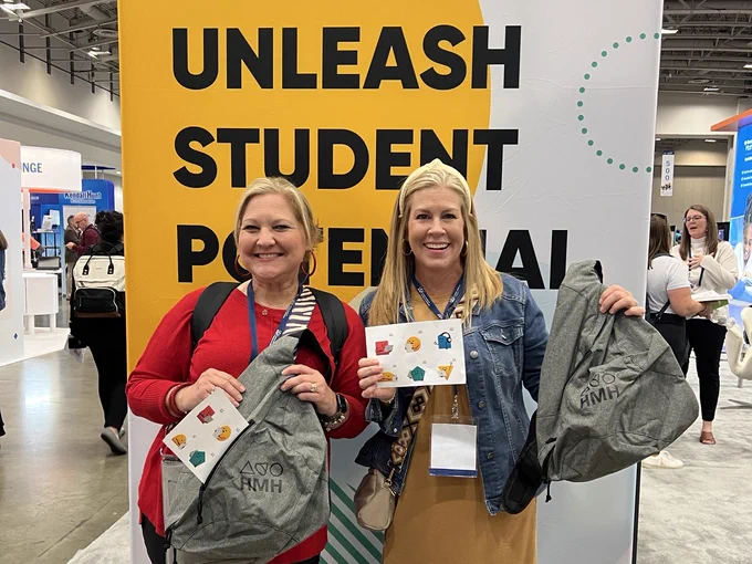 Two blonde women pose in front of a sign that reads: Unleash Student Potential. They are holding backpacks and smiling.