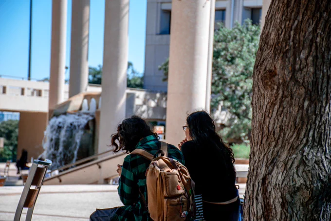 Two students sit on a bench in Sombrilla Plaza.
