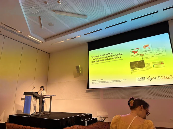 Hwiyeon Kim, wearing a light jacket and jeans, at the podium. The screen shows the title “Towards Visualization Thumbnail Designs That Entice Reading Data-Driven Articles”.