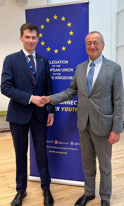 Maurizio and EU Ambassador Pedro Serrano posing for a photo with an EU Delegation banner in the background.