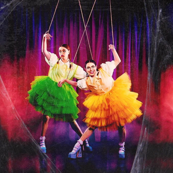 The two character comedians who make up Siblings. They both wear large tutus and have their arms in the air with string coming down,as if they are puppets. There are cobwebs round the edge of the image. 