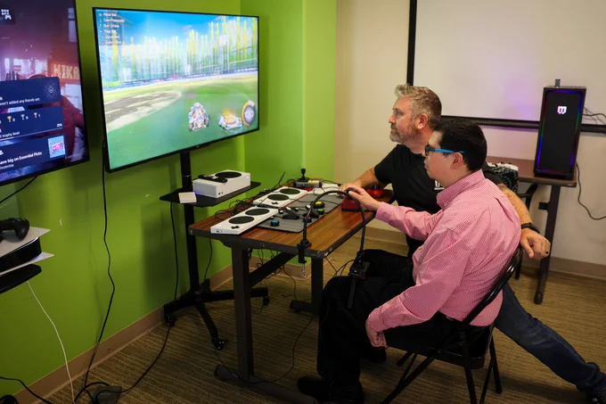 Erik instructing a client how to play with an adaptive gaming setup. He's playing Rocket League on the xbox