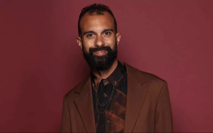 ATC Artistic Director Matthew Xia smiles to camera, wearing a red jacket and a deep red shirt, pictured against a red background