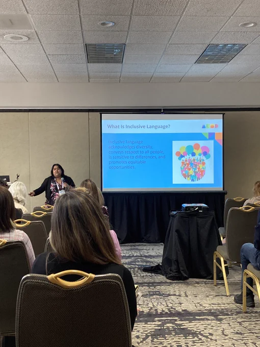 Photo of the conference presentation with the speaker with a slide titled “What is inclusive language?” and the text Inclusive language acknowledges diversity, conveys respect to all people, is sensitive to differences, and promotes equitable opportunities”