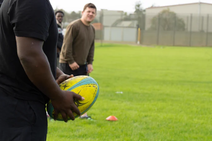 Photograph of an unidentifiable rugby player preparing to throw the rugby ball to Michael Crofts, CEO of 3Pillars Project in the background. 