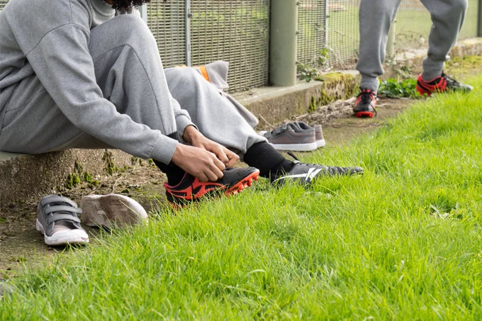 Photograph of an unidentifiable young person sitting on the ground lacing their rugby boots up.