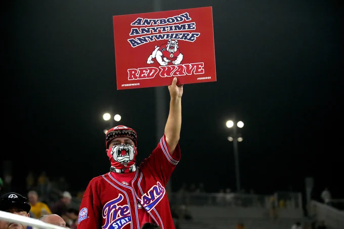 A Fresno State fan uses the Bulldog logo to cover part of his face like a mask while holding a sign that reads, "Anybody, Anytime, Anywhere. Red Wave."