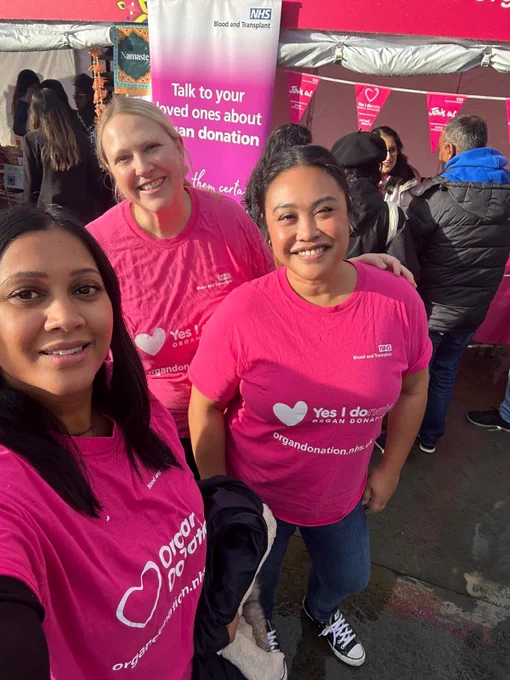 Specialist nurses in organ donation Nisha, Tamara and Lucy in their pink organ donation T-shirts stand in front of their stand raising awareness
