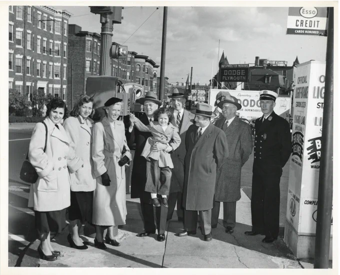 	Pictured in photograph, from left to right: Miss Leonard (President, Student Council, Roxbury Memorial High School), Miss Vengron (President, Senior Class, Roxbury Memorial High School), Miss Callahan (Head of History Department, Roxbury Memorial High School), Mayor Hynes holding Anne Marie Fink (2 Savin Street, Dorchester), Commissioner Reilly, Councillor Milton Cook, Robert Masterson (Headmaster, Roxbury Memorial High School for Boys), and Captain Marley (Boston Fire Department).