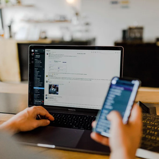 Image of a person using a laptop while also holding and using a smartphone.