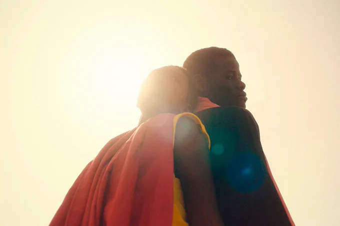 Two people stood against the sun with their backs against each other. 
