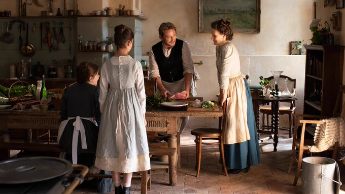 Four people stand around a long wooden table in a kitchen. On the table are piles of ingredients ready to be chopped. 
