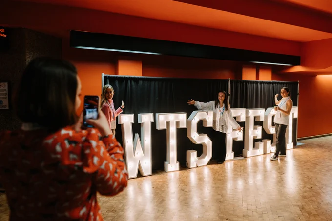 One woman taking a picture of three women by the WTSFest light sign