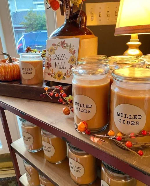 A shelf in a store holds mulled cider-scented candles and a sign that reads “Hello fall.”
