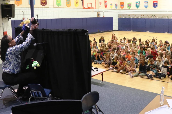 A Rockwood administrator leads a puppet show about friendship in a school gymnasium.