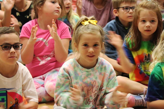 A Rockwood student smiles and claps during a puppet show about friendship in her school gymnasium.