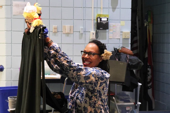 A Rockwood administrator smiles as she leads a puppet show about friendship in a school gymnasium.