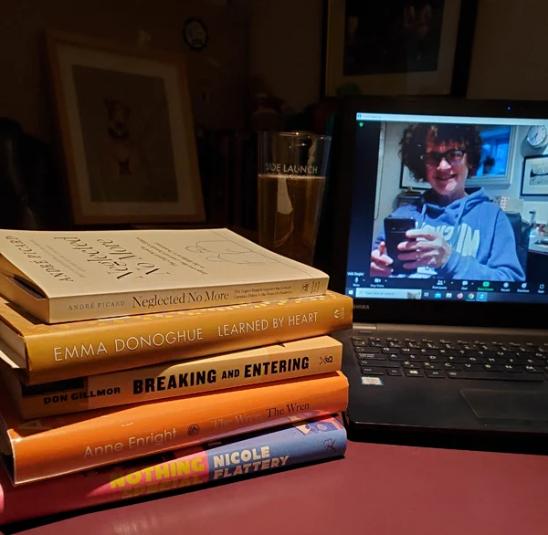 Silent book club member Vicki (that's me) on-screen, getting ready for a zoom meeting, with a stack of books, including The Fraud by Zadie Smith, next to her computer