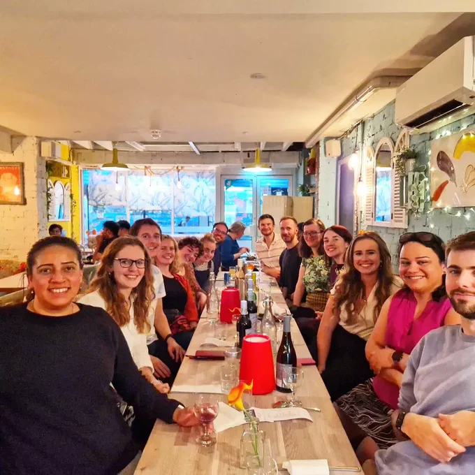 A group of people sit in a restaurant along a table.