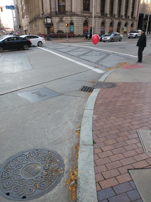 a single red balloon floats above a catch basin sewer grate on the curb of a downtown cleveland intersection.