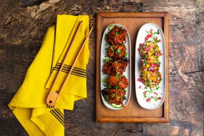 Food photography featuring onion bhajis on a wooden table with a yellow kitchen towel next to it.