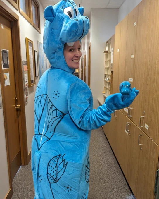Person in a blue hippo costume holding a small ceramic blue hippo