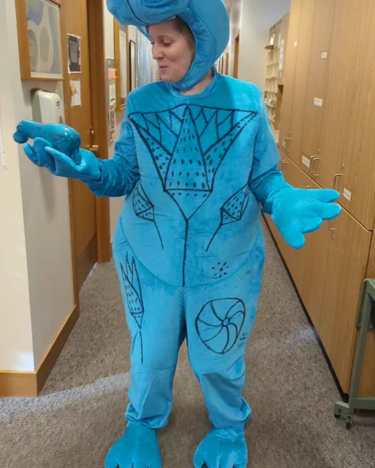 Person in a blue hippo costume holding a small ceramic blue hippo
