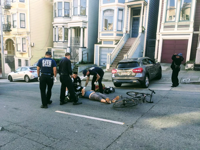 SFFD attending to a cyclist on the ground after being hit by a driver pulling out of a driveway