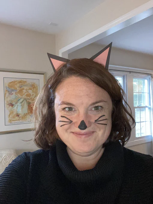 Selfie of me wearing a black turtleneck sweater, with black and pink construction paper cat ears and a nose and whiskers drawn on my face with black eyeliner.