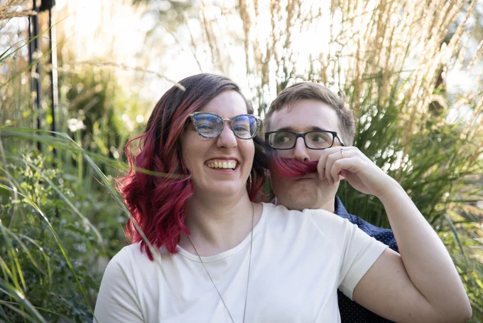 Me and Alex: I'm wearing a white shirt and my hair (brown and red) is curled, I'm holding a strand of my hair up over Alex's mouth like a mustache and he's making a funny face. I'm laughing.