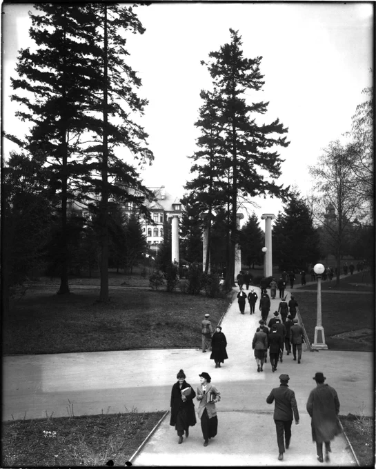 Black and white film photo shows young men and women walking through a college campus.
