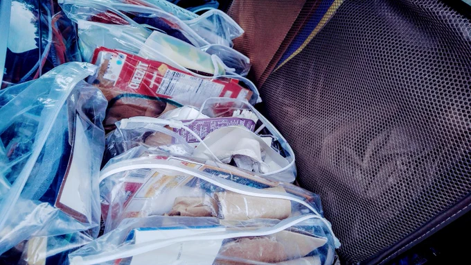 Close up of an open suitcase full of zip-top plastic bags that are filled with bits of cardboard and other 'junk'.