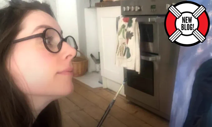 New blog! A picture of Rhiannon Vivian holding a small paint brush, looking at a painting.